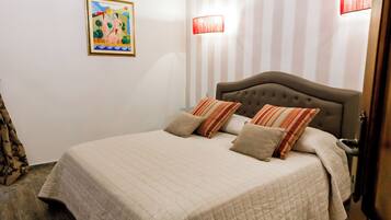 A bedroom with a bed, a chandelier, striped wallpaper, and a painting on the wall.