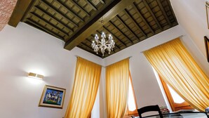 A room with a wooden ceiling, a chandelier, yellow curtains, a framed picture on the wall, and a table with chairs.