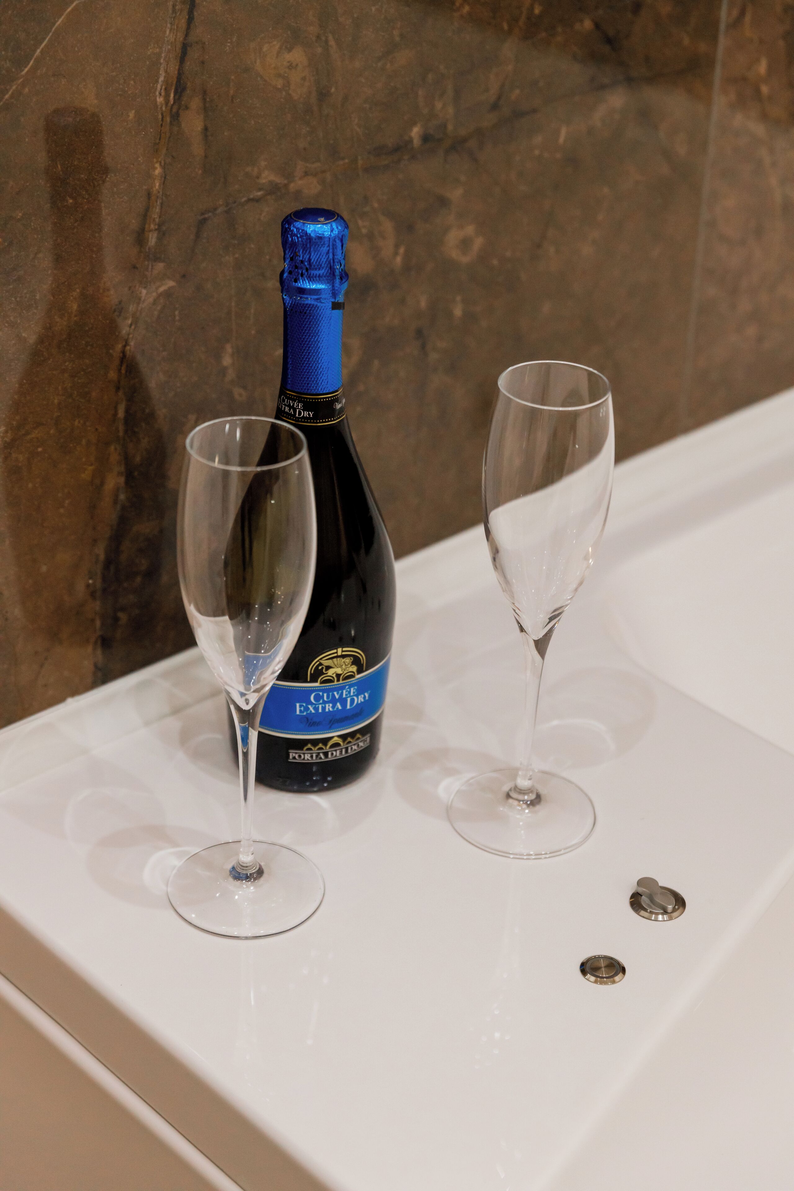 Een fles Cuvée Extra Dry champagne en twee lege glazen op een wit oppervlak met een marmeren achtergrond.