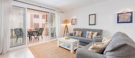Una sala de estar moderna con un sofá gris, una mesa de centro blanca y un comedor con sillas y una mesa.