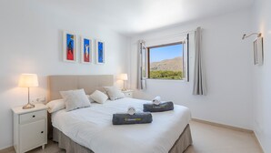 Ein ordentlich eingerichtetes Schlafzimmer mit einem großen Bett, zwei Nachttischen mit Lampen und Bildern an der Wand.
