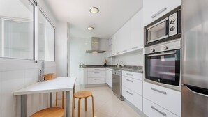 Eine moderne Küche mit weißen Schränken, Edelstahlgeräten und einem Holzhocker.