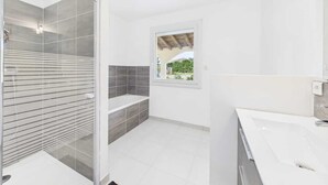 A modern bathroom with a glass-enclosed shower, a bathtub, and a large window. - The 3 arcades (Ucel)