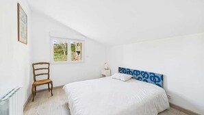 A bedroom with a bed, a chair, a nightstand, a window, and a radiator. - The 3 arcades (Ucel)