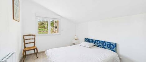 Un dormitorio con cama, una silla, una mesita de noche, una ventana y un radiador.