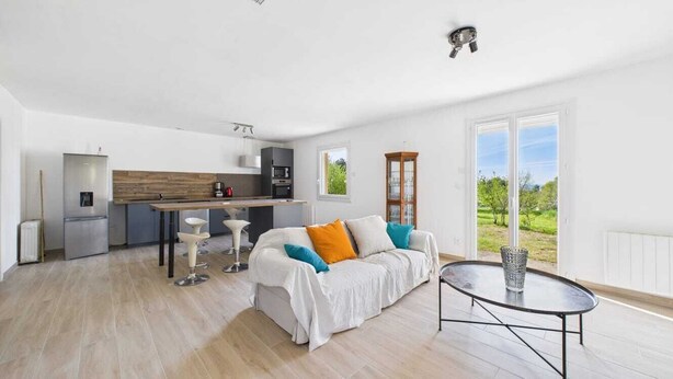 A modern apartment with a kitchen, a dining area, a living room with a sofa and a coffee table, and a large window with a view of greenery. - The 3 arcades (Ucel)
