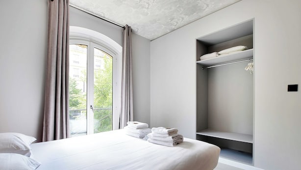 Ein Hotelzimmer mit Bett, einem Vorhangfenster, einem eingebauten Kleiderschrank mit Regalen und Blick auf Grünfläche.