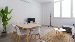 Ein modernes Wohnzimmer mit Essbereich, einem großen Fenster, einem Kleiderständer und einer Topfpflanze.