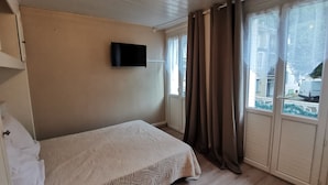 A bedroom with a bed, a television mounted on the wall, and a window with curtains. - Studio with bike room (Bagnères-de-Luchon)