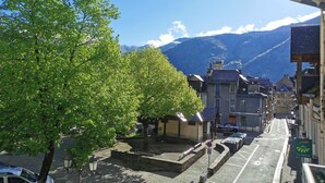 A street view with a tree-lined sidewalk, parked cars, and a mountain backdrop. - Studio with bike room (Bagnères-de-Luchon)