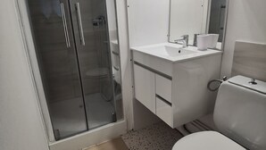 A bathroom with a glass-enclosed shower, a white sink with a mirror above, and a toilet. - Studio with bike room (Bagnères-de-Luchon)