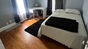 Een slaapkamer met een bed, een bureau en twee ramen met gordijnen.