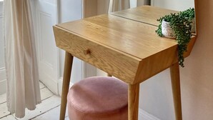 Une coiffeuse en bois avec un miroir, un tiroir et un tabouret rose.