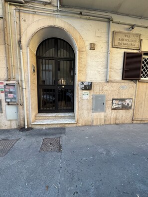 A building entrance with a large arched doorway, a black door with a metal grille, and a sign above the door indicating 'VIA Q VIII Bartolino da Novara.' - Lt_Panella Yellow Pop lovely apartment (Roma)