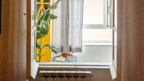 Vista a través de una puerta abierta que da a una habitación con radiador, una planta y una ventana con cortinas.