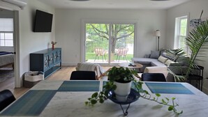 A modern living room with a dining area, large windows, and a view of a pond.