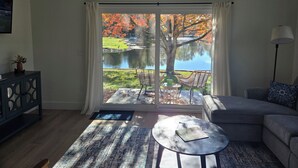 A living room with a large sliding glass door leading to a lake view, a sofa, a coffee table, and a lamp.