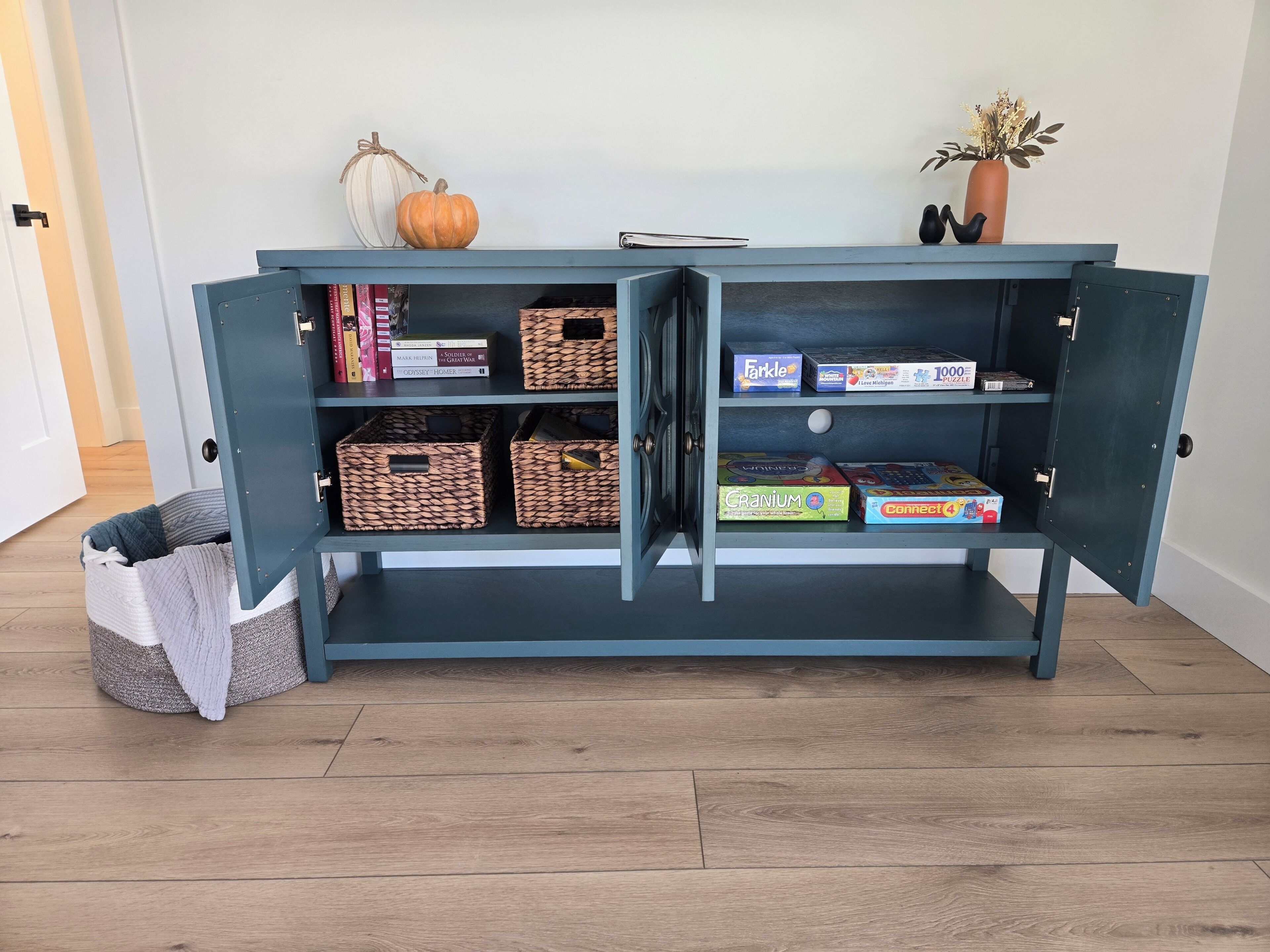 A blue cabinet with open shelves containing books, board games, and storage baskets.