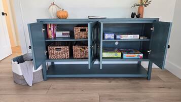 A blue cabinet with open shelves containing books, board games, and storage baskets.