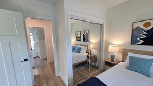 A hotel room with a bed, bedside tables, a mirror, and artwork on the wall.