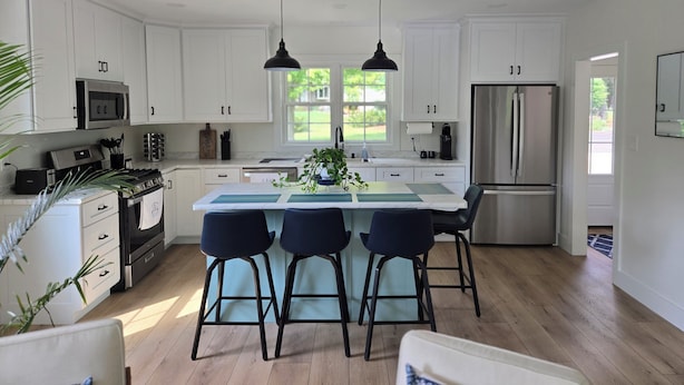 A modern kitchen with white cabinets, stainless steel appliances, a central island with bar stools, and pendant lighting.