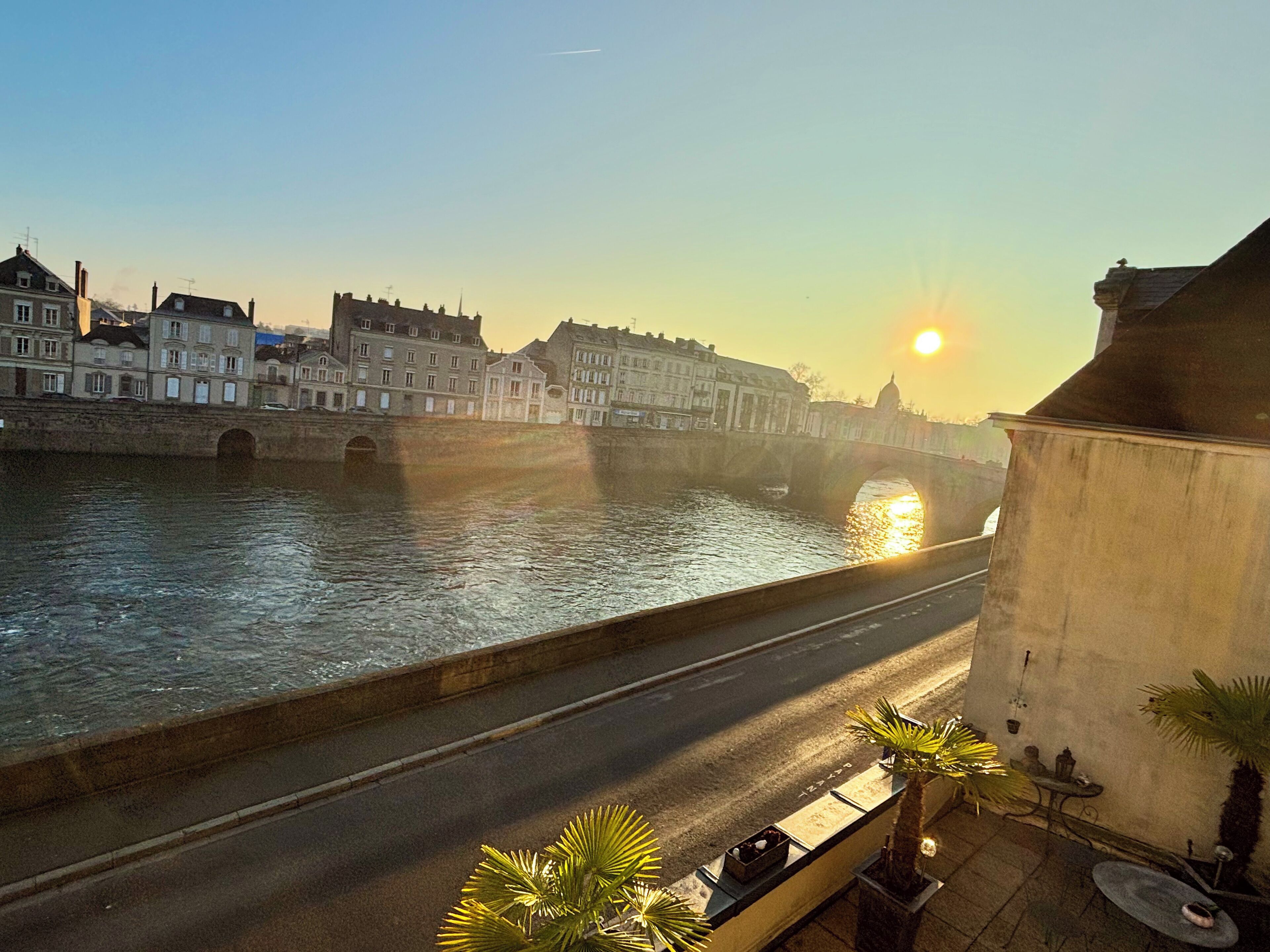 Une vue sur le fleuve, avec un pont, des bâtiments et un coucher de soleil.