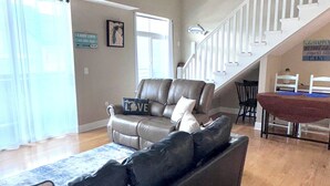 A living room with a leather sofa, a ceiling fan, a staircase, and a dining area. - Spacious Grand Haven Getaway (Grand Haven)