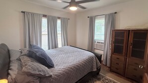 Un dormitorio con cama, ventilador de techo, armario y ventana con cortinas.