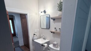 Un baño con inodoro, lavamanos, espejo y un pequeño estante con una planta.