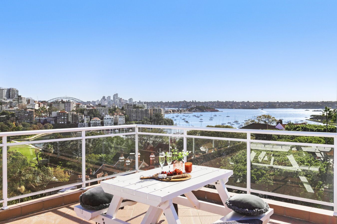 A balcony with a table set for two, overlooking a cityscape and a bay with boats.