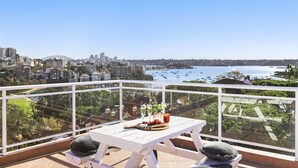A balcony with a table set for two, overlooking a cityscape and a bay with boats. - Stylish Studio with Rooftop Harbour Views (Darling Point)
