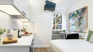A compact hotel room with a kitchenette, a bed, a small seating area, and a large abstract painting. - Stylish Studio with Rooftop Harbour Views (Darling Point)