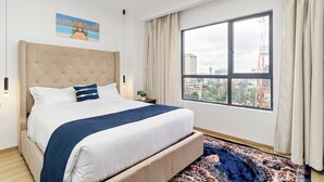 Une chambre d’hôtel avec un grand lit, une vue sur la ville, un tapis à motifs et un tableau au mur.
