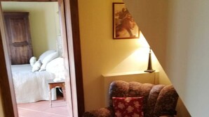 Un couloir avec une chaise et une lampe, qui mène à une chambre à coucher avec un lit et une porte.