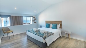 Una camera da letto moderna con un letto grande, vista sul mare attraverso una finestra e un piccolo comodino.