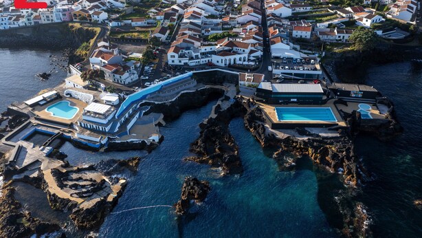 Una vista aerea di una cittadina costiera con un porto turistico, costa rocciosa e edifici residenziali.