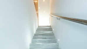 Una scala con finitura in legno, pareti bianche e corrimano a destra.