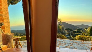 A view from a room with a large glass door leading to an outdoor patio with a tiled floor and a view of a mountainous landscape. - Parc du Montnegre, villa with magnificent sea view (Tordera)