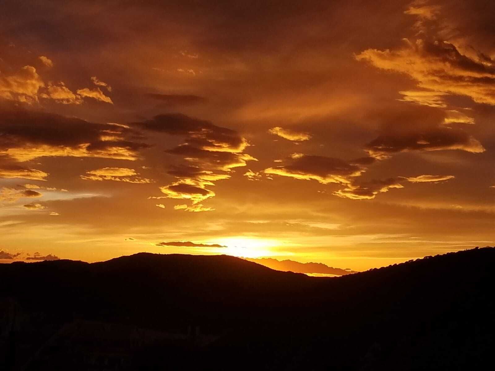 Ein Sonnenuntergang über einer Berglandschaft mit den Silhouetten von Hügeln und einem klaren Himmel.