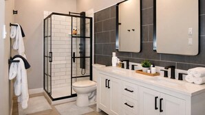 Et moderne badeværelse med en glasvægs brusekabine, toilet, vask med spejl og et underskab med skabe.
