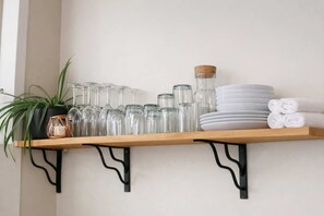 A shelf with glassware, plates, and towels.