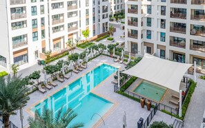 Un immeuble résidentiel à plusieurs étages doté d’une piscine centrale, d’un espace extérieur aménagé et de verdure.