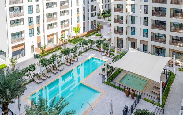 A multi-story residential building with a central swimming pool, outdoor seating, and greenery.