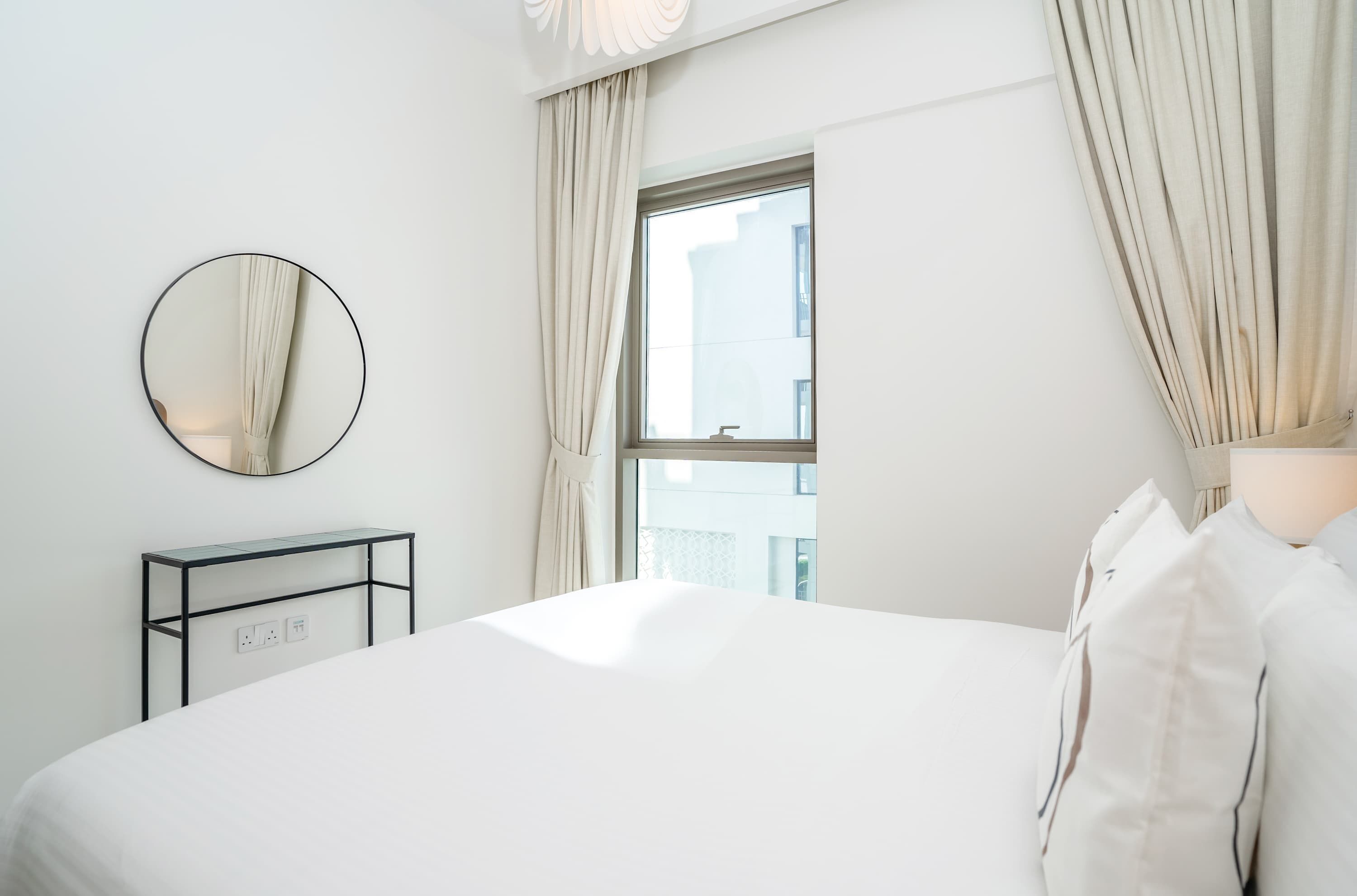 Ein Hotelzimmer mit einem Bett, einem runden Spiegel, einem Nachttisch mit Steckdose und einem Vorhangfenster.
