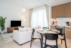 A modern living room with a sofa, TV, dining table, chairs, kitchen area, and a potted plant.