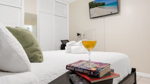 Ein ordentlich bezogenes Bett mit Fernbedienung, einem Weinglas und einem Buch mit dem Titel 'UNTAMED GLENNON DOYLE' auf einem Nachttisch.