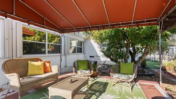A covered patio area with wicker furniture, a table, and a potted plant.