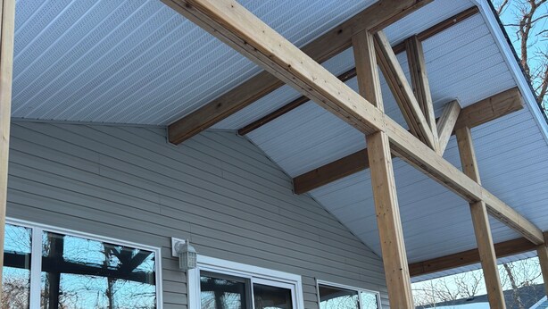 Une terrasse en bois avec une rambarde, un espace porche couvert et une vue sur une maison avec des fenêtres.