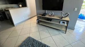A modern living room with a flat-screen TV mounted on the wall, a wooden entertainment unit below, and a kitchen area in the background. - Cozy 2-bedroom condo with AC, WiFi in wonderful Las Vegas with strip view (Las Vegas)