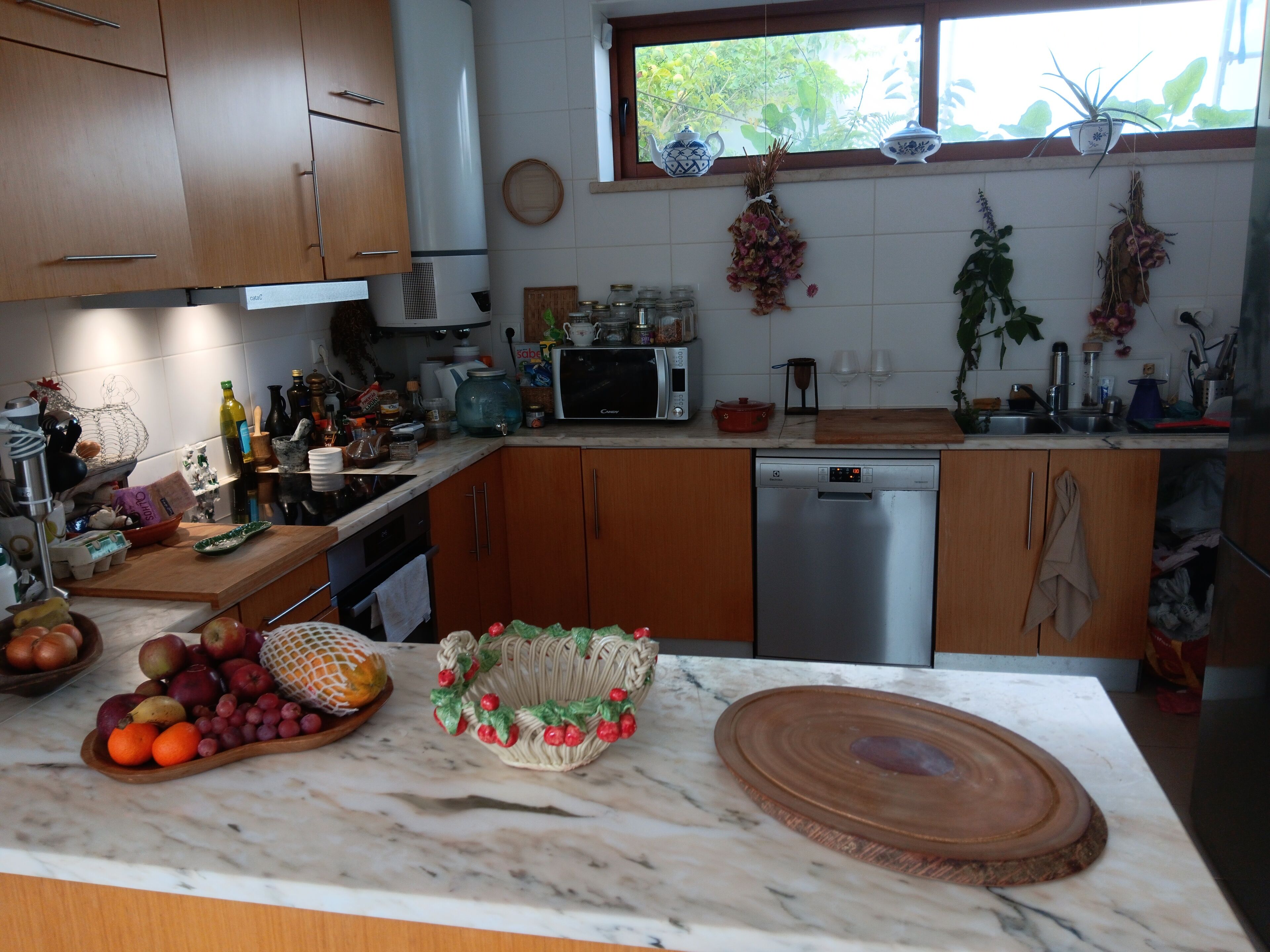 A kitchen with wooden cabinets, a dishwasher, a microwave, and a sink. There are various kitchen items and a fruit bowl on the counter.